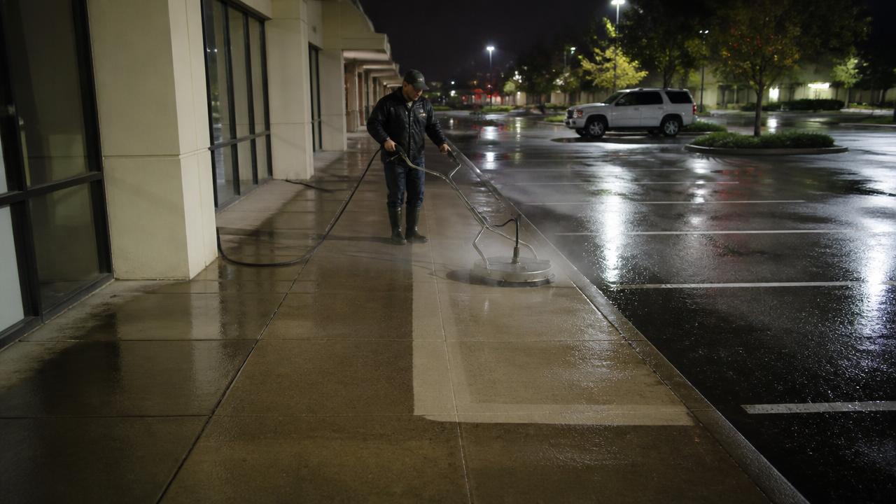 Overnight pressure washing of a retail center sidewalk showing a clean stripe against stained concrete